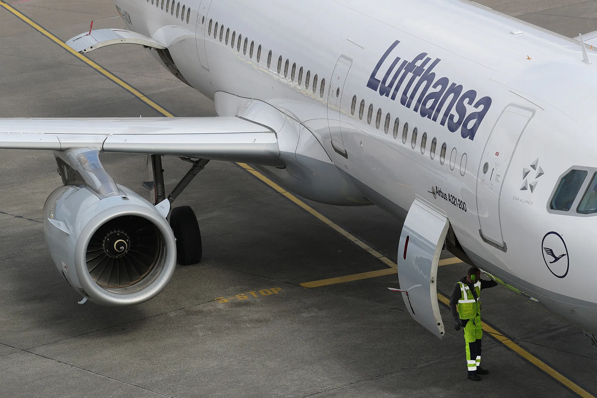 A ground crew member stands beneath an Airbus A321 aircraft, operated by Deutsche Lufthansa.