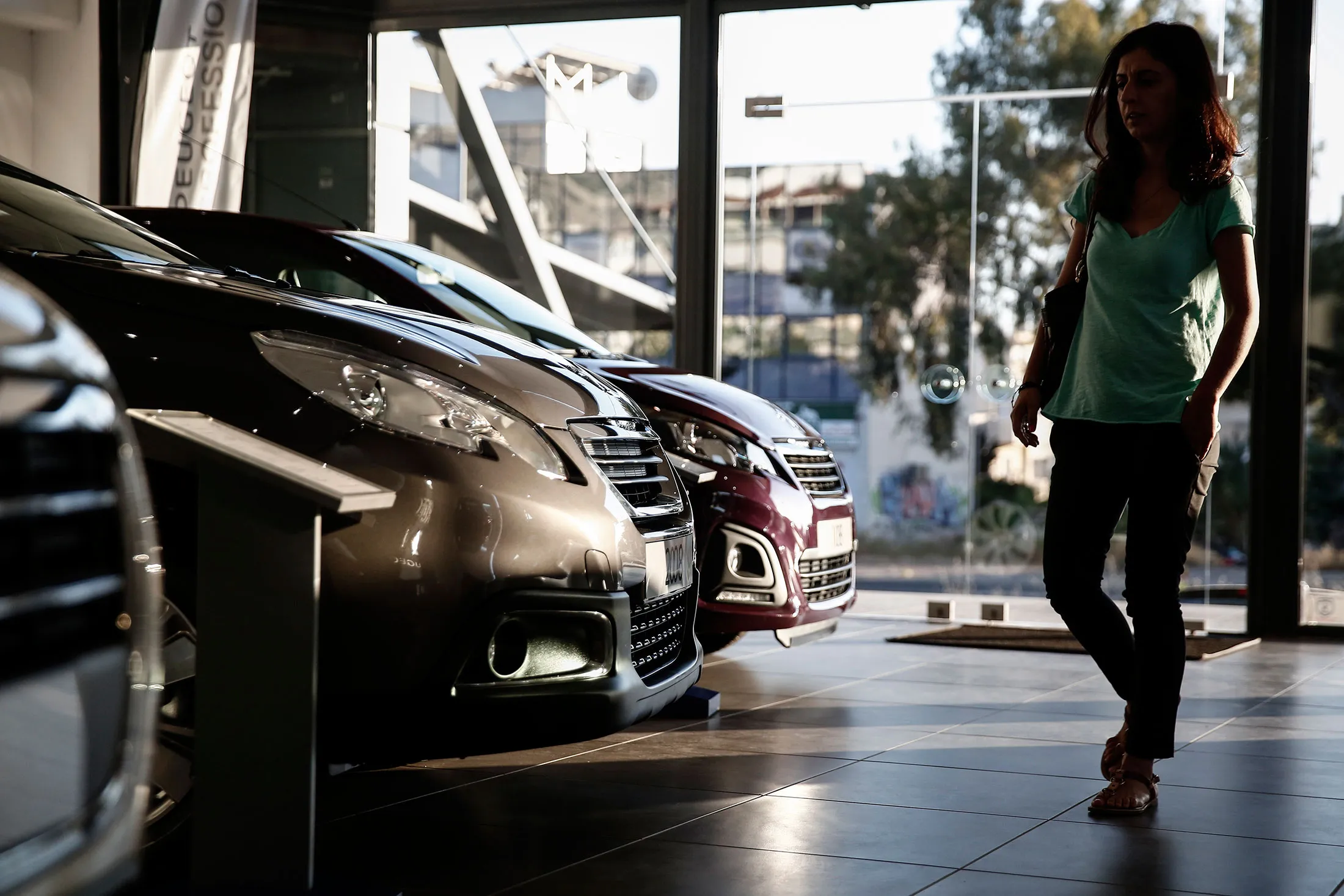 A visitor passes new PSA Peugeot Citroen vehicles for sale at the Kaliantasis automobile dealership in the Glyfada district of Athens.
