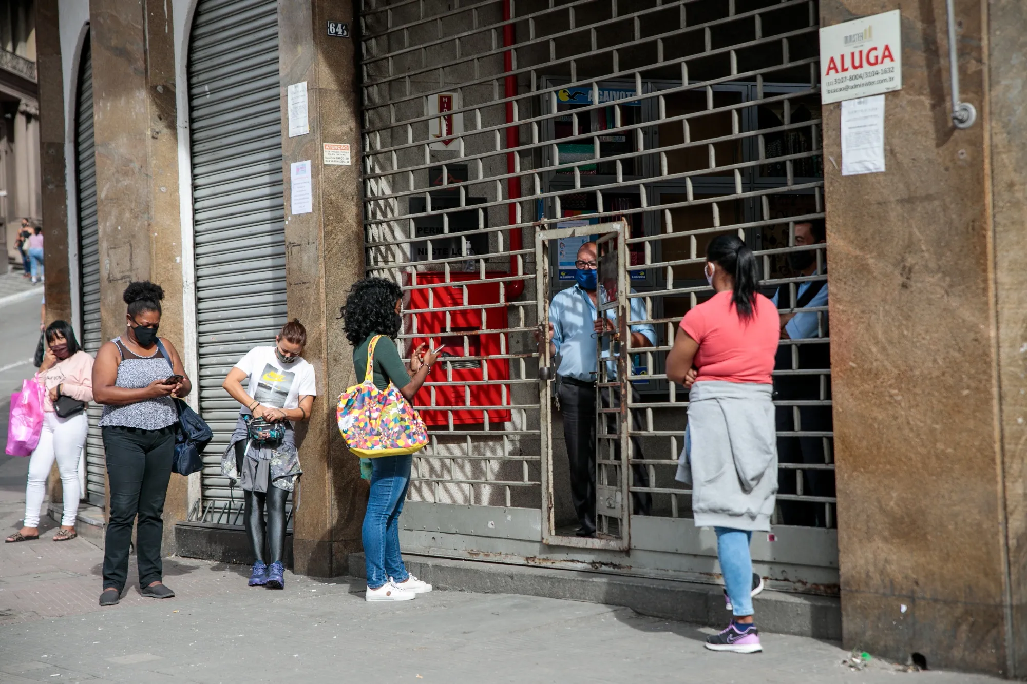 People wearing protective masks wait outside a street mall prior to official opening hours in downtown Sao Paulo on June 10.