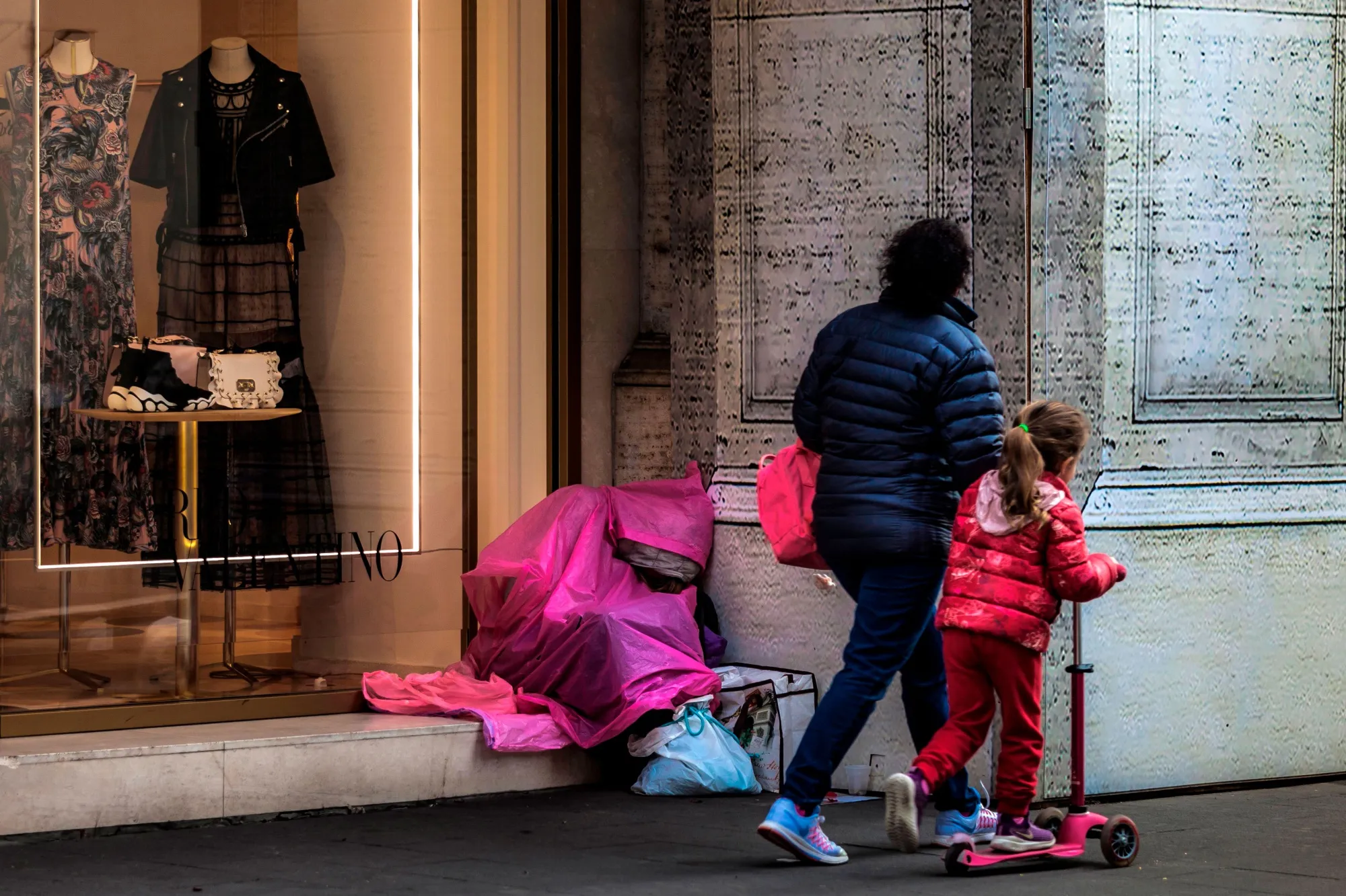 Pedestrians walk past a homeless person in Rome.