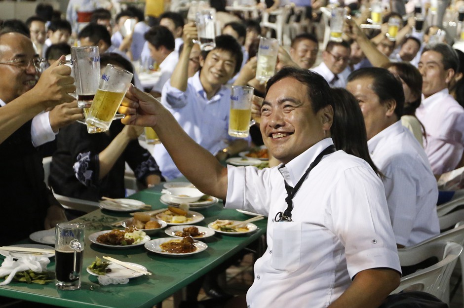 Employees of a Tokyo company raise beer mugs in a toast at an after-work party. 