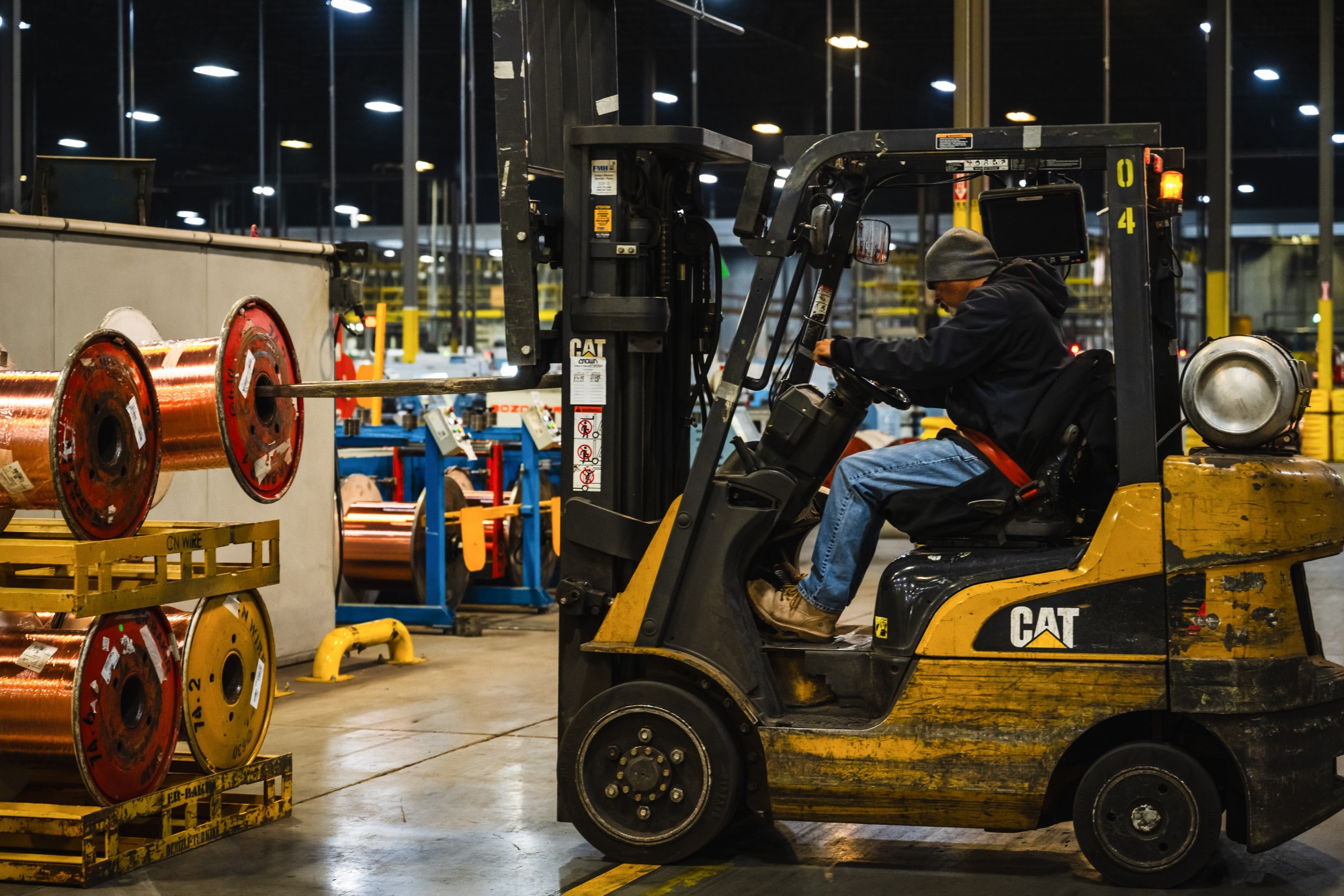 A worker moves spools of copper wire between rod breakdown machines.