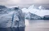 A picture of icebergs floating in a tranquil sea. The icebergs look pristine white, covered with a thick layer of snow.