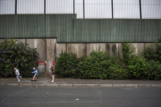 Children play hopscotch on the pavings of a nationalist area that runs alongside a peace wall separating the unionist and nationalist communities, in West Belfast, Northern Ireland, U.K., on Thursday, July 8, 2021. Britain's departure from the European Union has exposed fault lines across the U.K. and no more so than Northern Ireland, where Brexit highlighted the often violent split between pro-U.K. unionists and nationalists wanting to unite the island of Ireland.