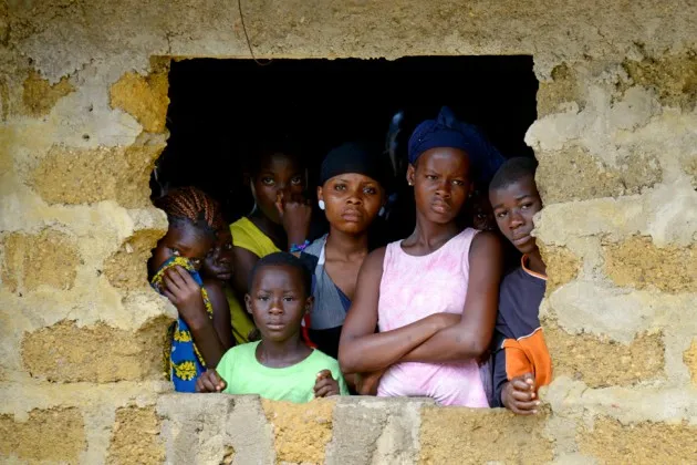 Local residents watch as an Ebola victim is transported away by aid workers in Banjol, Liberia