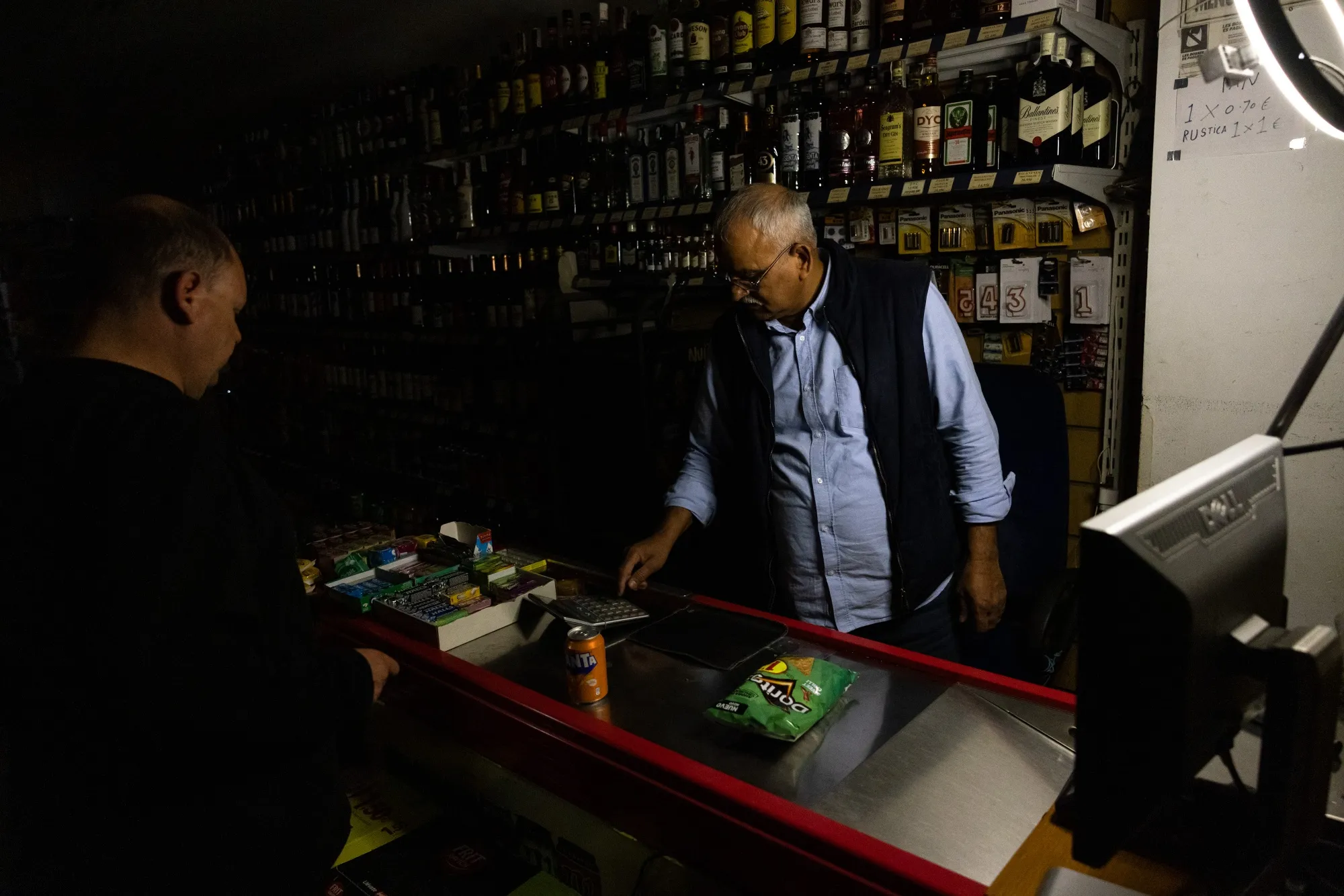 A shop owner calculates a customer's bill using a calculator during a power outage in Barcelona.