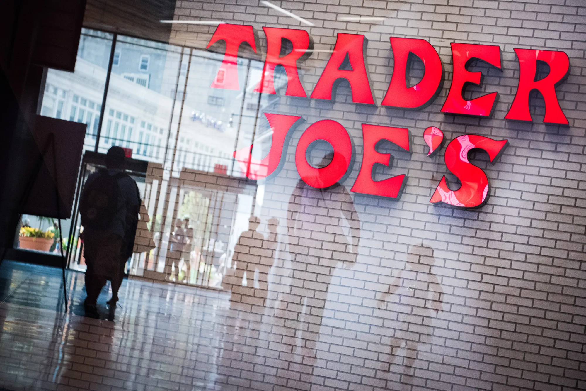 Shoppers are reflected in a window in front of Trader Joe's grocery store signage at City Point in the Brooklyn borough of New York, U.S., on Tuesday, July 18, 2017.&nbsp;