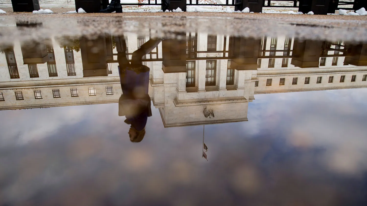 A woman walks past the Marriner S. Eccles Federal Reserve building as it is reflected in a puddle of water in Washington, D.C., U.S., on Tuesday, Jan. 27, 2015.

