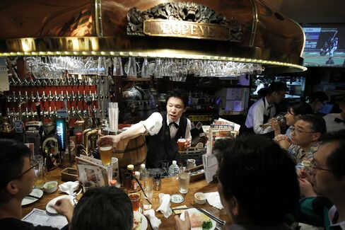 A bartender, center, serves glasses of craft beer to customers sitting at the bar of the Bakusyu Club Popeye in the Ryogoku neighborhood of Tokyo, on May 1, 2015. Photographer: Kiyoshi Ota/Bloomberg