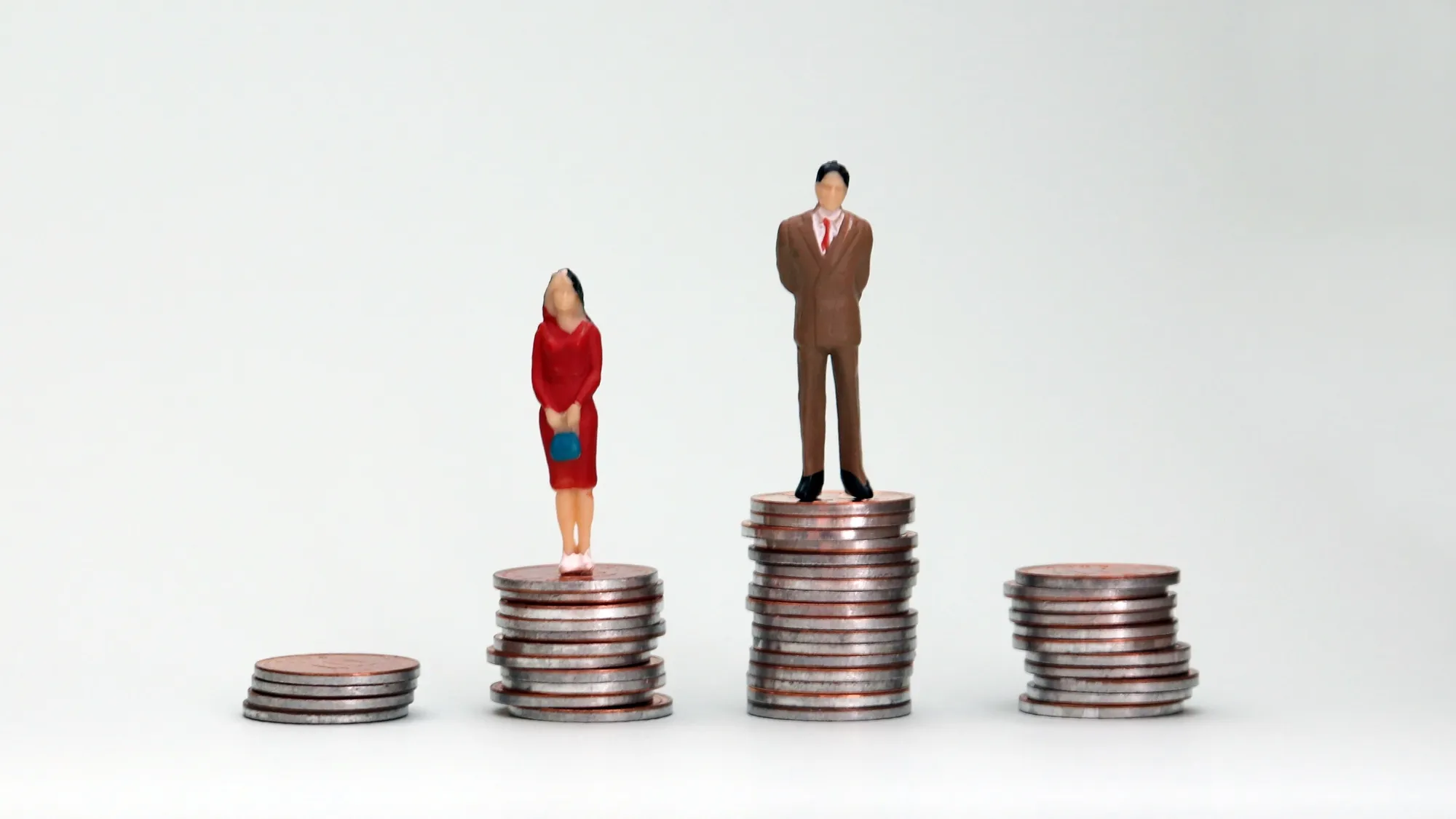 Gender wage difference concept. A miniature man and a woman standing on top of a pile of coins.