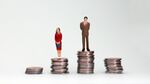 Gender wage difference concept. A miniature man and a woman standing on top of a pile of coins.