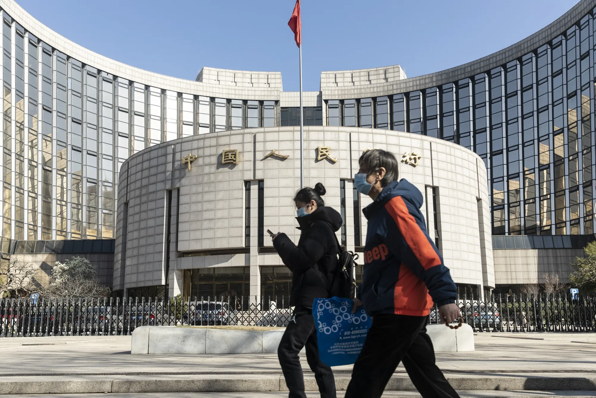 Pedestrians wearing protective masks walk past the People's Bank of China&nbsp;building in Beijing.
