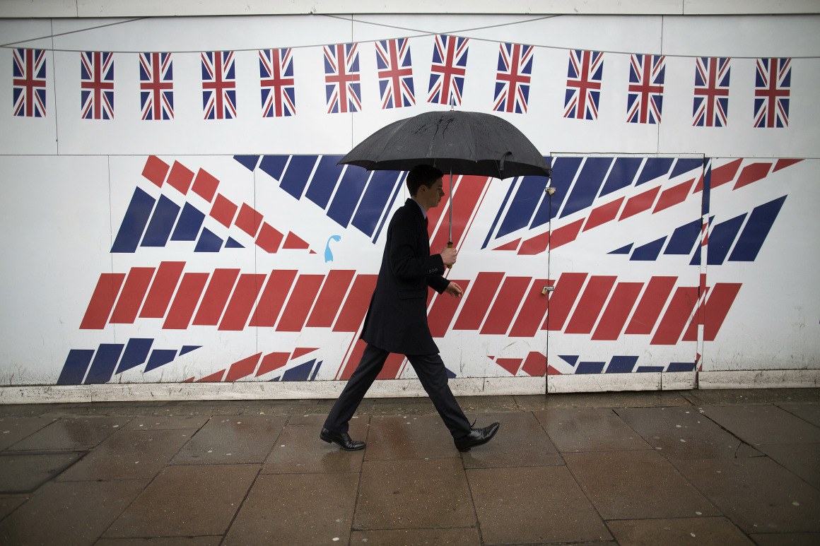 FILE: A pedestrian shelters from the rain beneath an umbrella as he passes construction hoardings decorated with British Union Jack flags in London, U.K., on Thursday, March 7, 2013. European Union and Jack flags as Brexit trade talks that were on the verge of a breakthrough descended into a fight between the U.K. and France on Thursday as the British government said prospects of an imminent deal had receded.