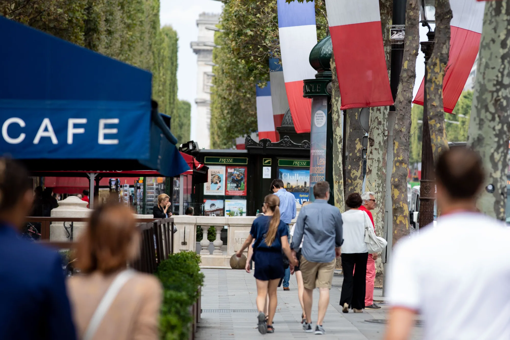 Pedestrians pass a cafe as French national flag banners hang along the Champs Elysee in Paris.