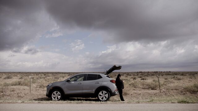Carol Barrios standing by the trunk of her vehicle looking at her phone on the side of the road