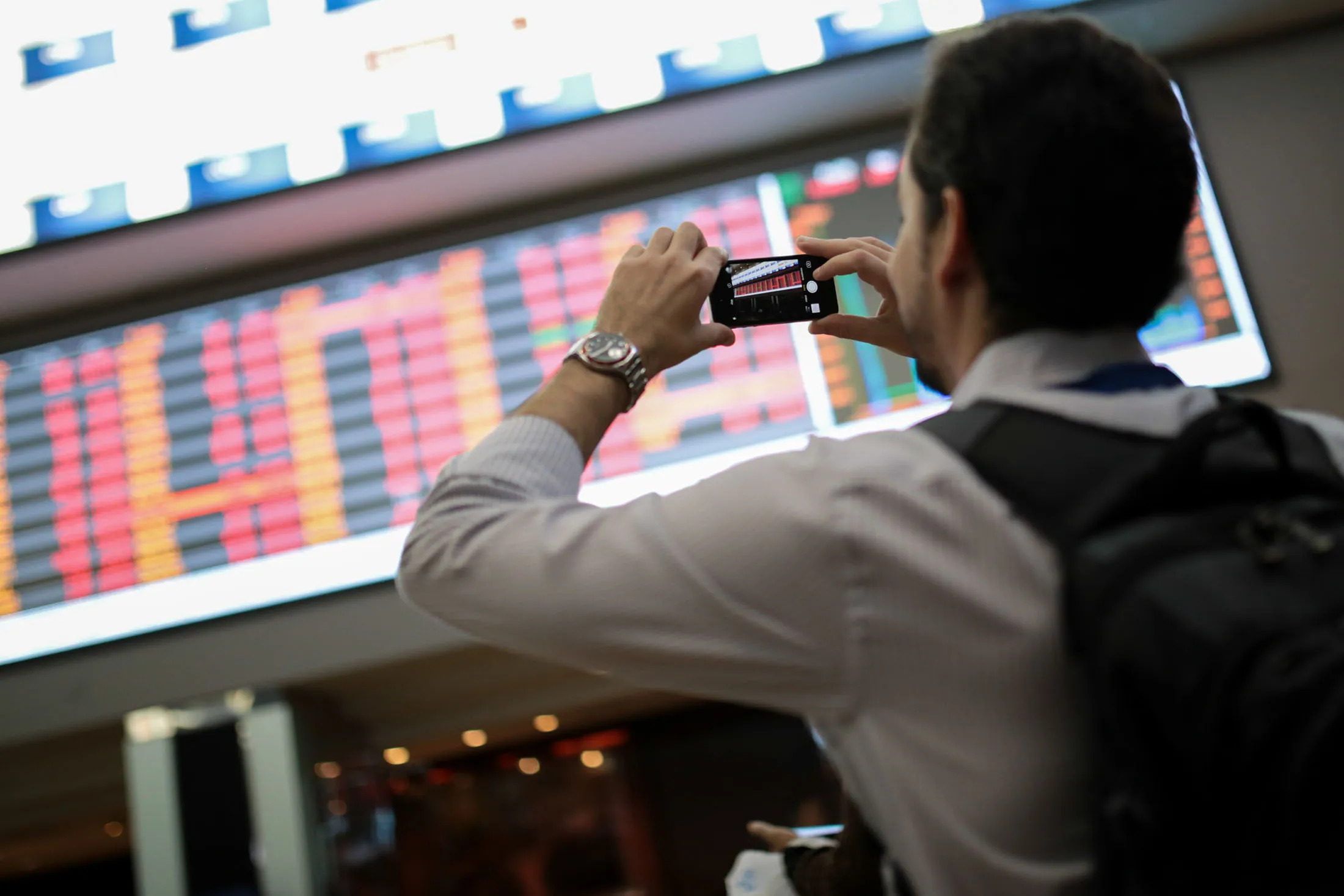 A visitor takes a photograph with a smartphone of the electronic board displaying stock activity at the Brasil Bolsa Bacao (B3) stock exchange in Sao Paulo, Brazil