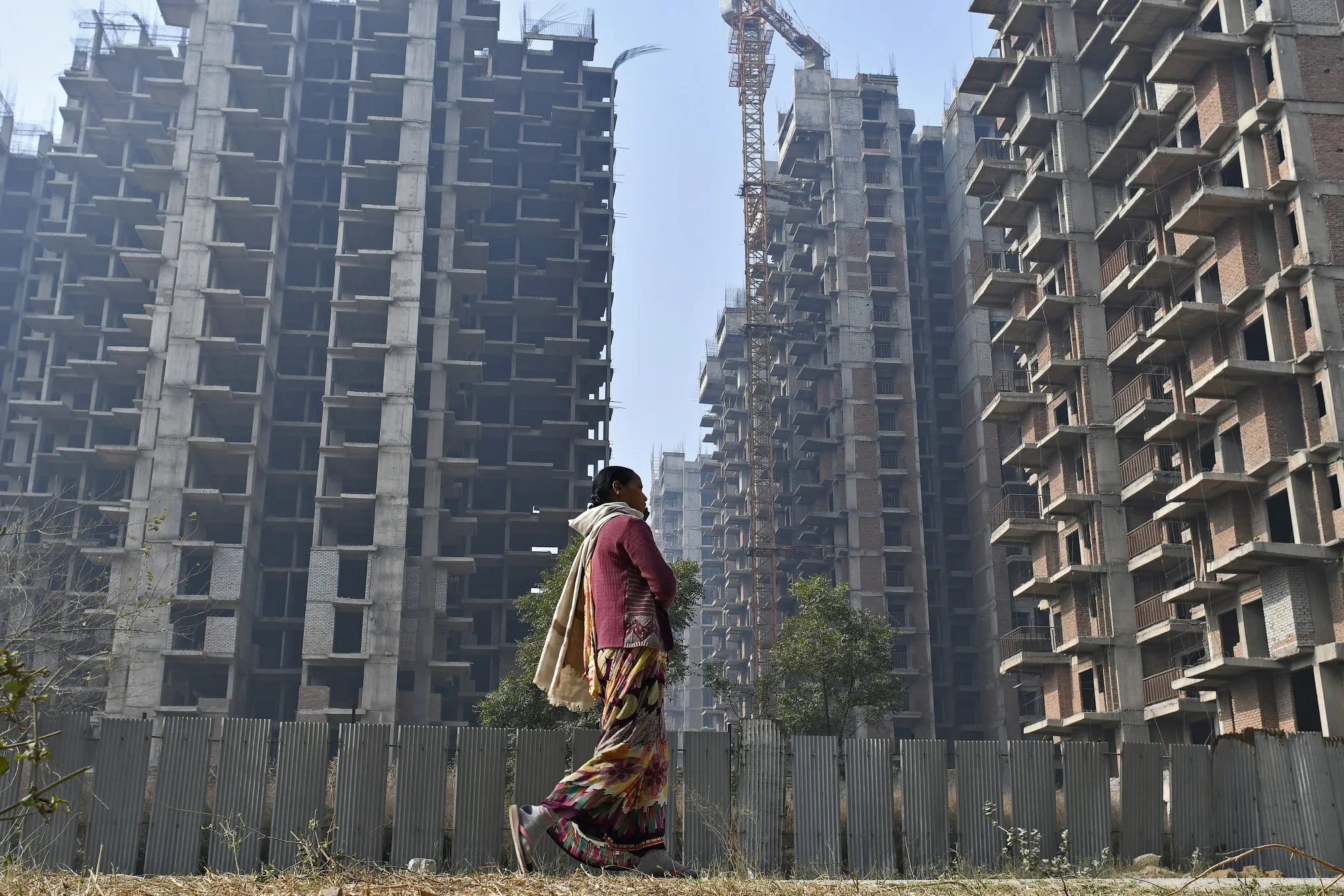 A pedestrian walks past residential buildings under construction in Uttar Pradesh, India.