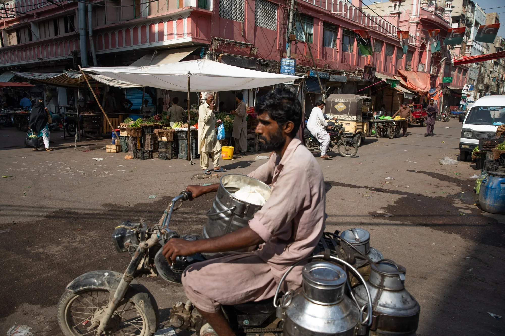 A motorcyclist transports milk churns through a market in Karachi.