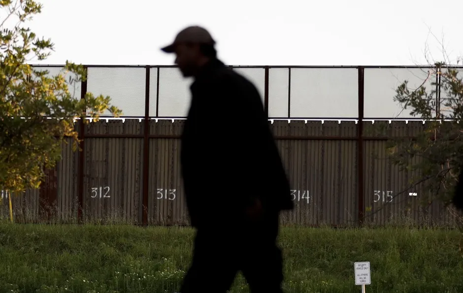 A man in San Diego passes in front of the border fence with Mexico. 