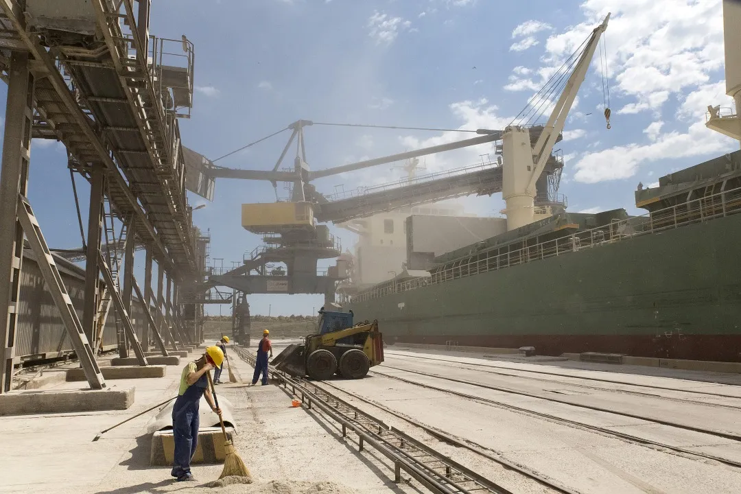 Workers sweep grain on the dockside during loading operations onto a cargo ship for export in Yuzhniy port.