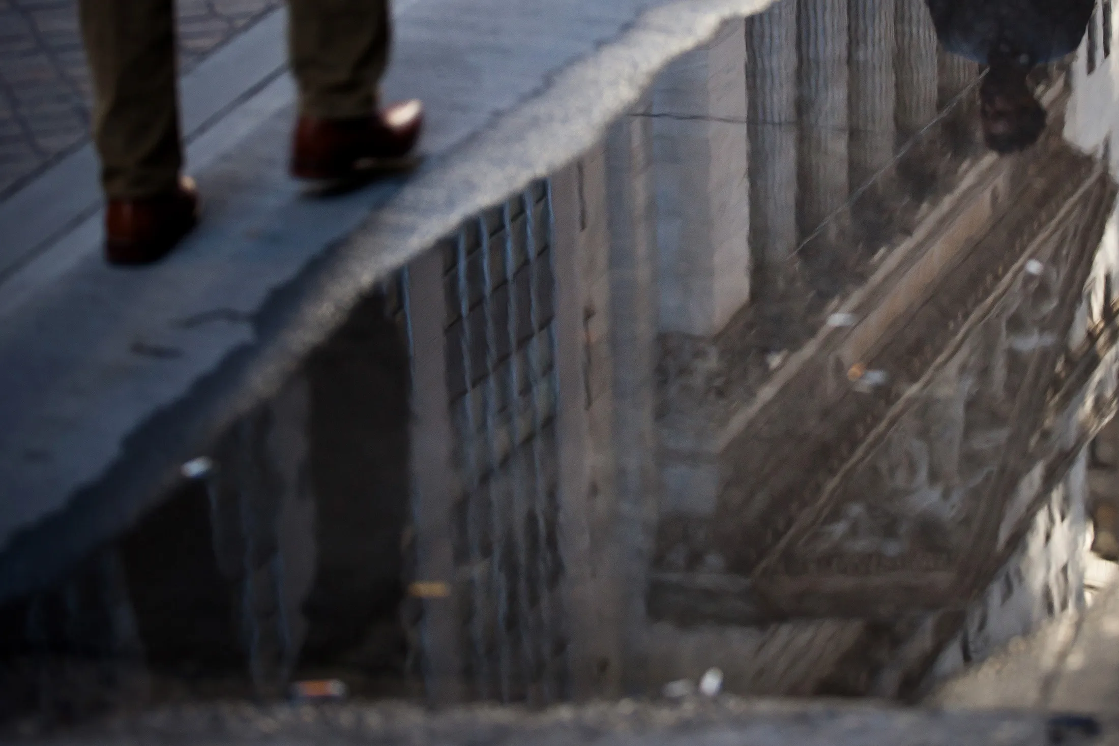 A pedestrian walks past a puddle reflecting the New York Stock Exchange.
