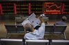 An investor reads a newspaper in front of screens showing stock market movements at a securities company in Beijing.