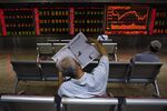 An investor reads a newspaper in front of screens showing stock market movements at a securities company in Beijing.