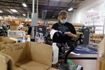 An employee wearing a protective masks reviews paperwork at the Gifts For You company warehouse in Woodridge, Illinois, U.S., on Monday, Aug. 24, 2020. 