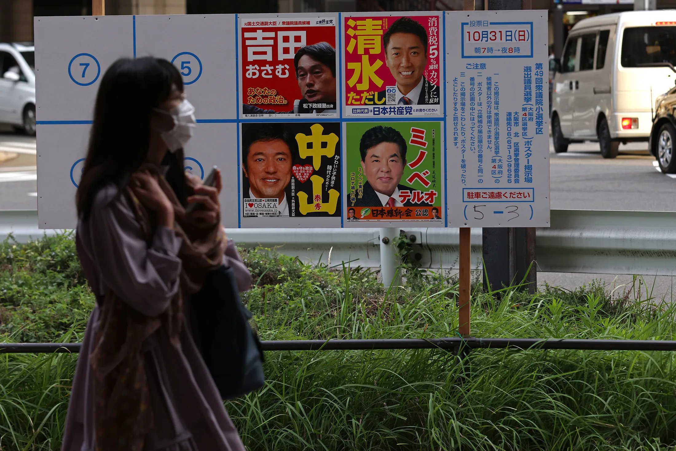 A woman wearing a protective face mask walks past candidate posters in Osaka on Oct. 19.