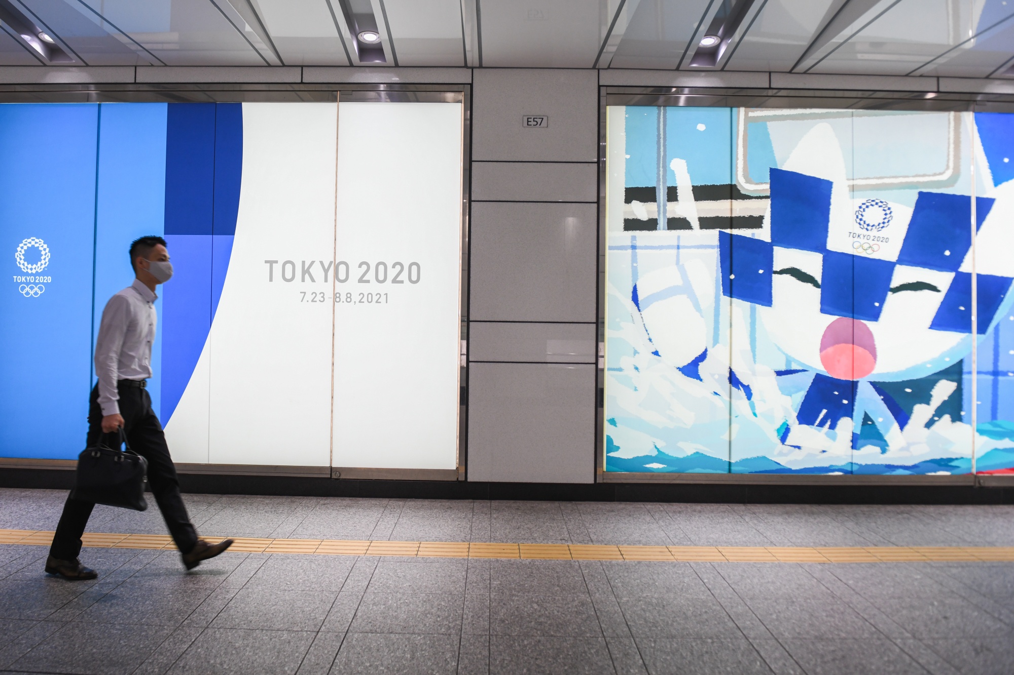 A pedestrian walks past a sign promoting the Tokyo 2020 Olympic Games near Shinjuku station in Tokyo, Japan, on Friday, June 18, 2021. 
