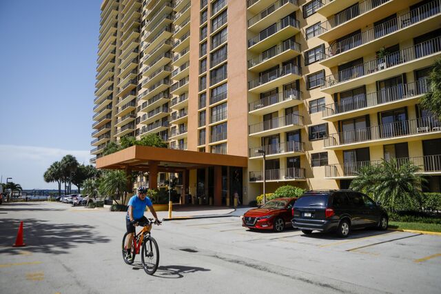 an older gentleman rides a bike past the front entrance of a yellow condo building