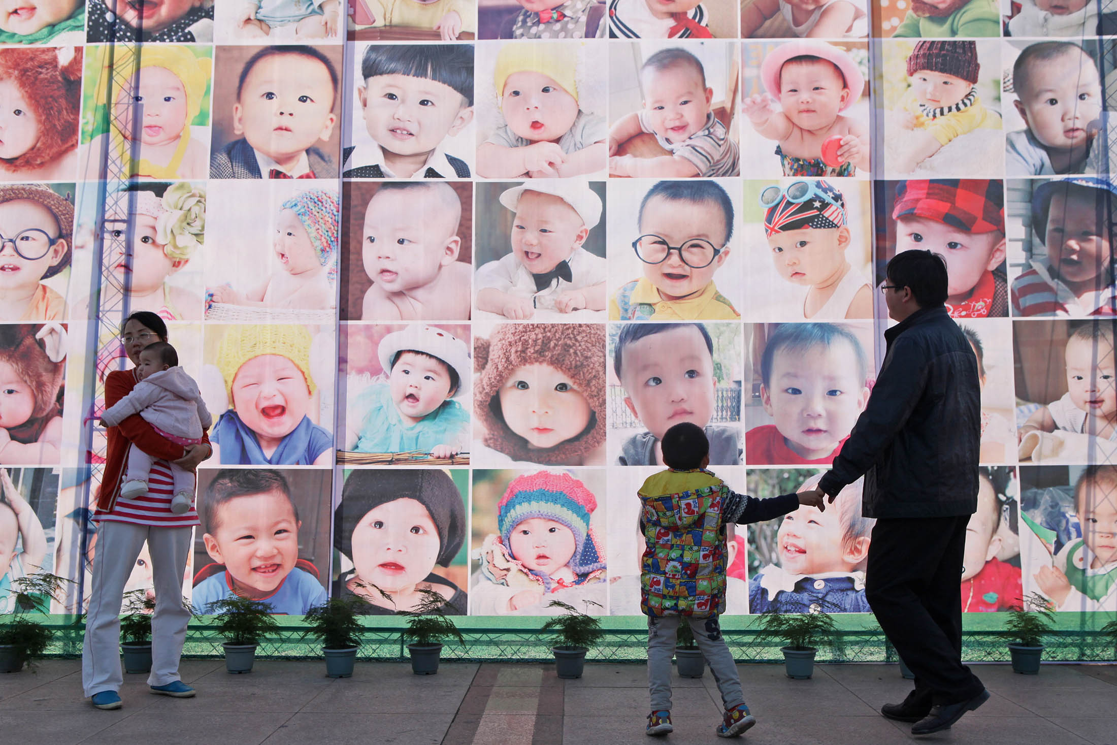 People pass a poster printed with faces of babies in Taizhou, Zhejiang Province of China. The Chinese government has said that allowing all families to have two children is likely to add three million newborns each year. Still, a baby boom isn’t guaranteed.
