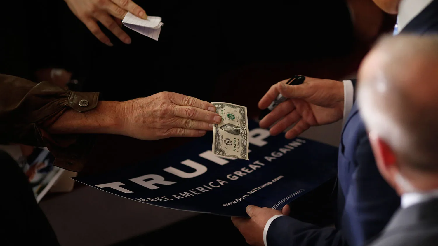 An attendee hands a $2 banknote to Donald Trump as Trump signs autographs in Gaffney, South Carolina, on Feb. 18, 2016.
