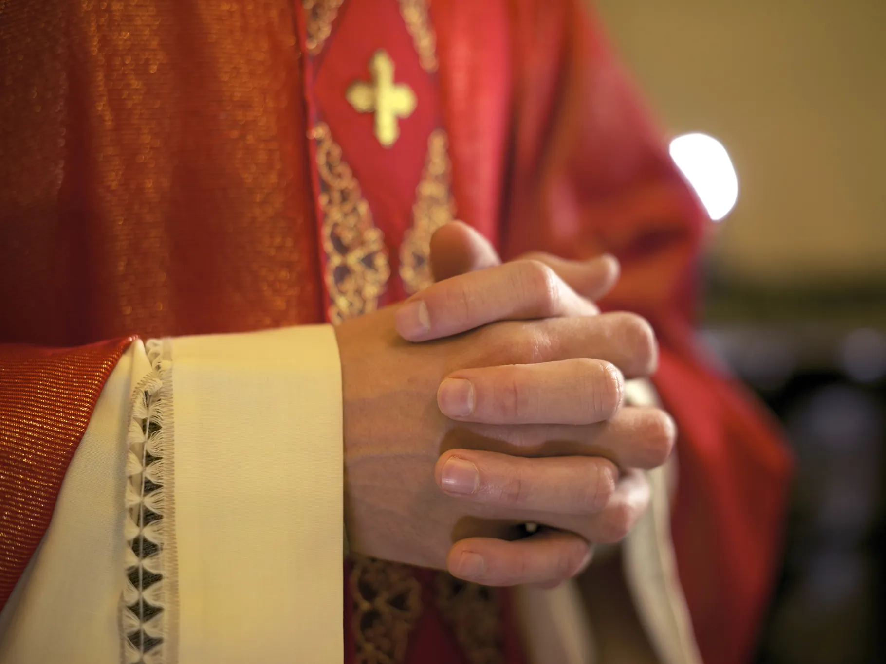 Catholic priest on altar praying with hands joined during mass service in church