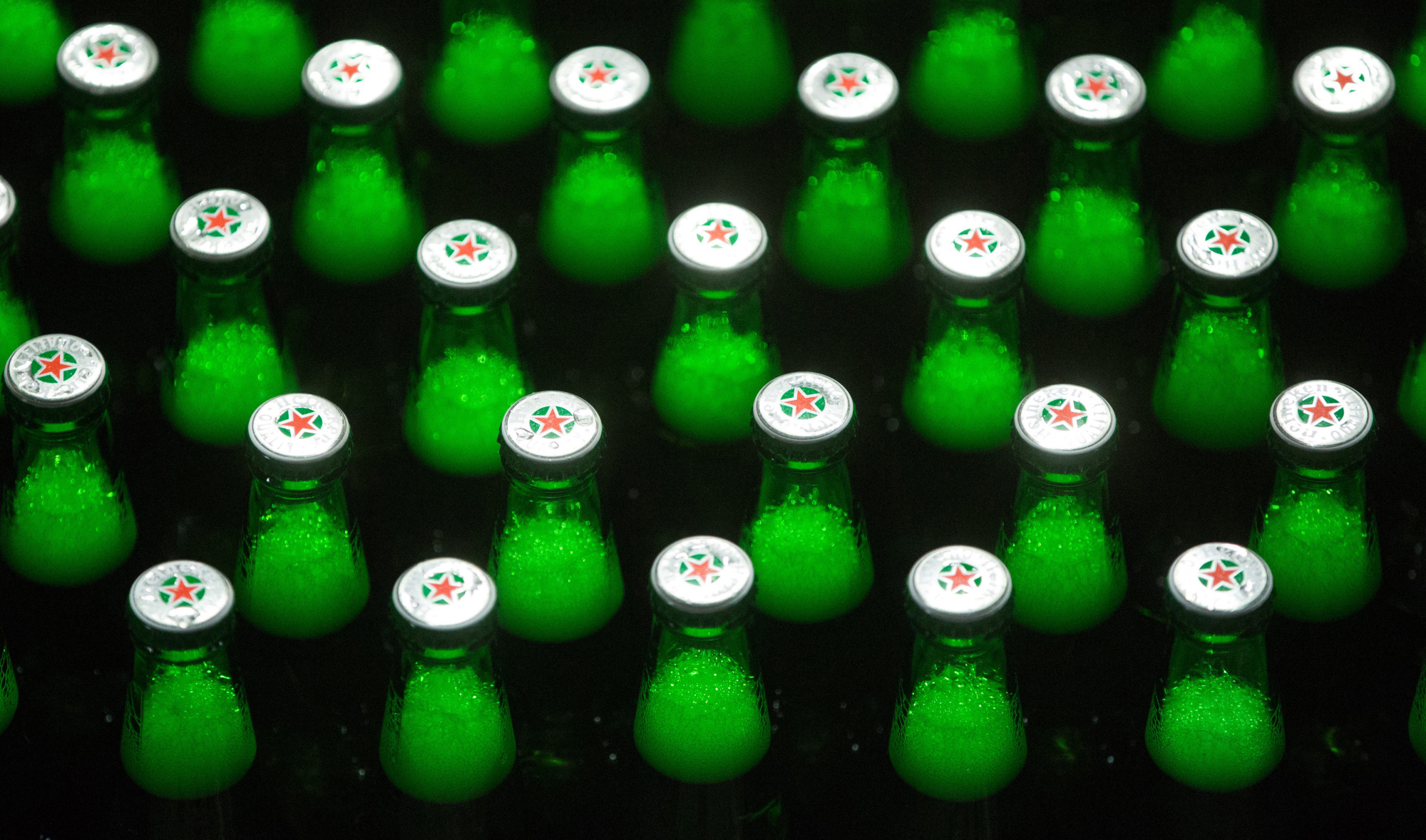 A Heineken logo sits on the bottle caps of Heinken beer as it travels along the production line at the Heineken NV brewery in Saint Petersburg, Russia, on Wednesday, Nov. 18, 2015.
