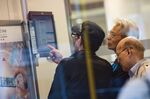 Customers look at a monitor displaying stock prices at a China Construction Bank Corp. branch.