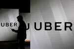 A man checks his smartphone whilst standing amongst illuminated screens bearing the Uber Technologies Inc. logo in this arranged photograph in London, U.K., on Tuesday, June 26, 2018.