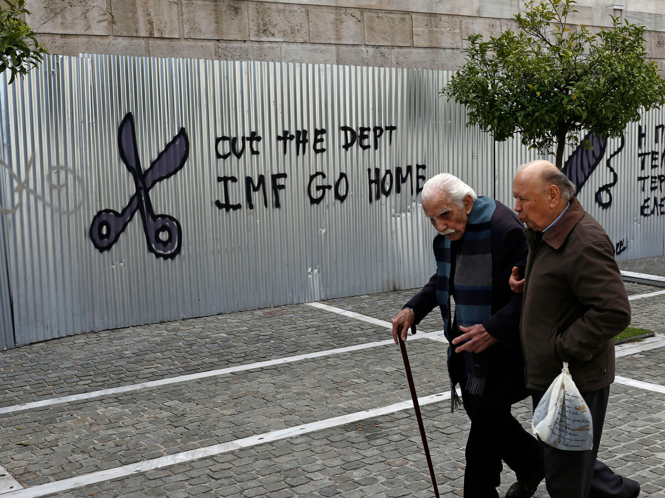 Two elderly men pass graffiti outside the University of Athens.
