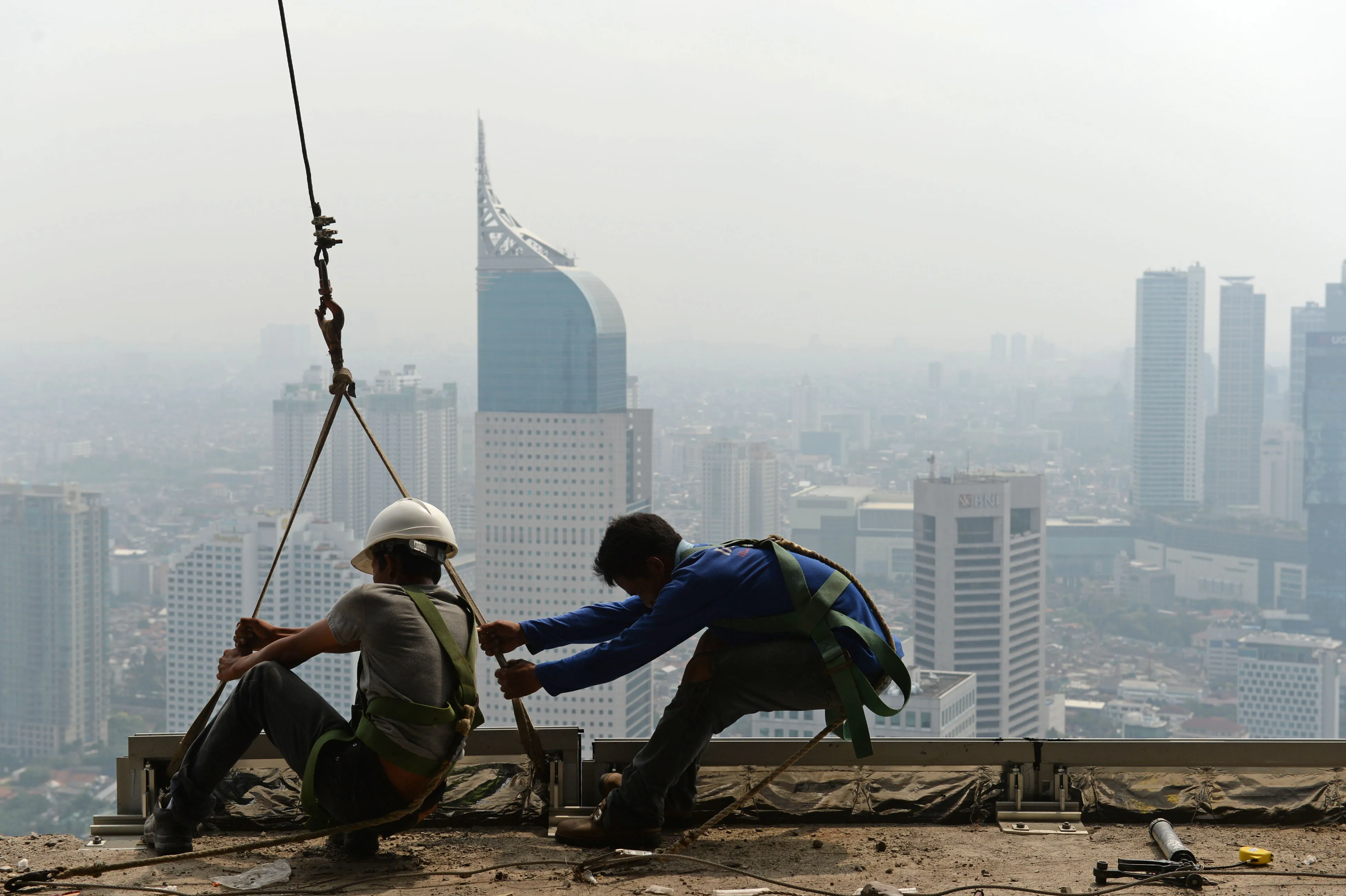 Construction workers labor on a building towering above the business district of Jakarta, Indonesia.