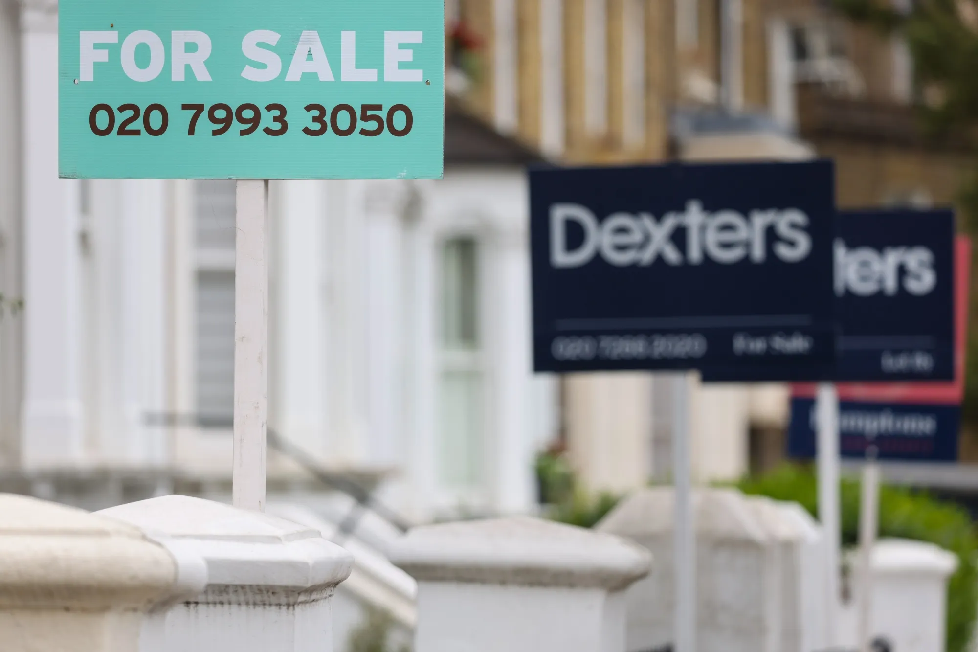 Estate agent "For Sale" signs outside residential properties in London.