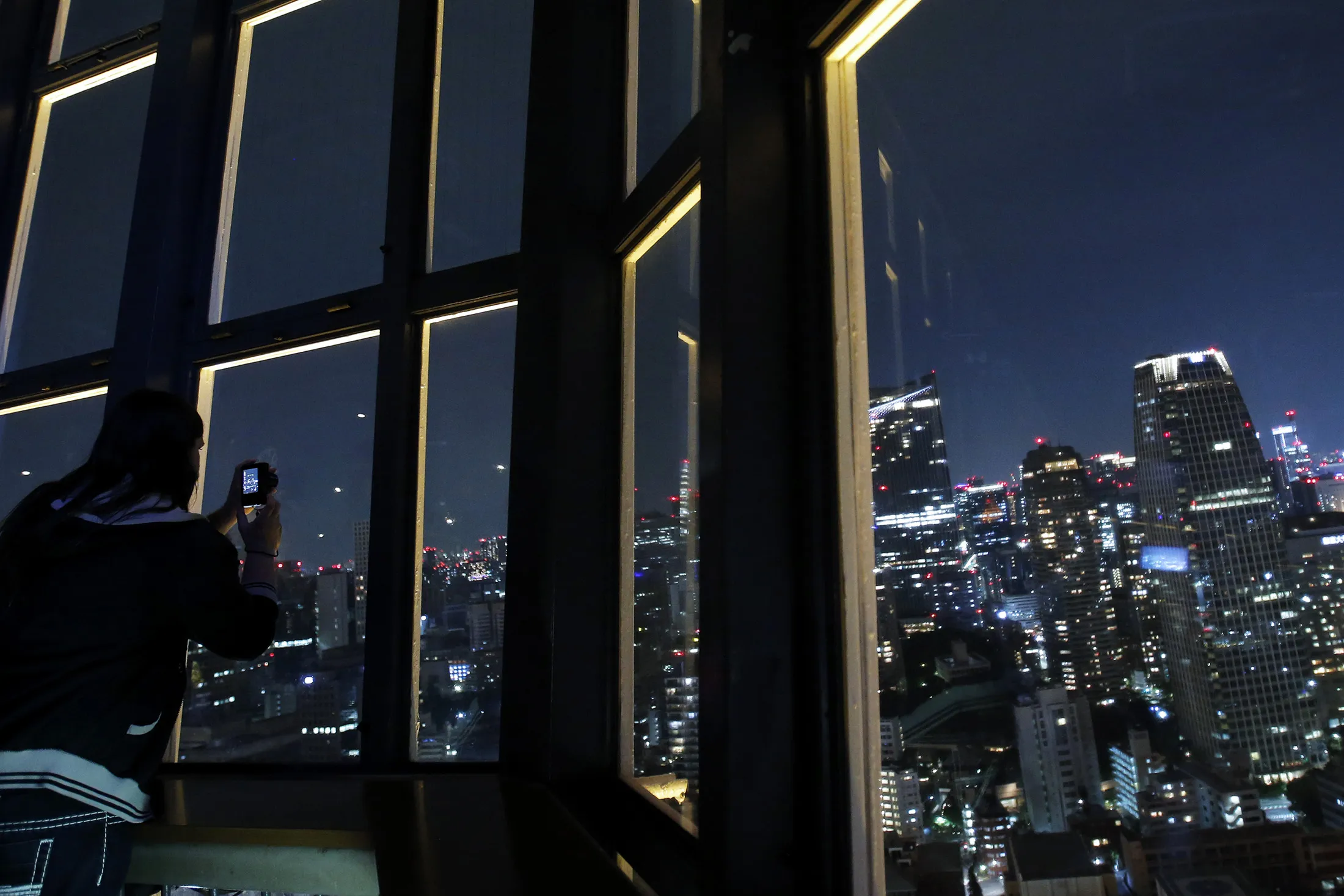 A person takes a photograph of the skyline from the observation deck of the Tokyo Tower.
