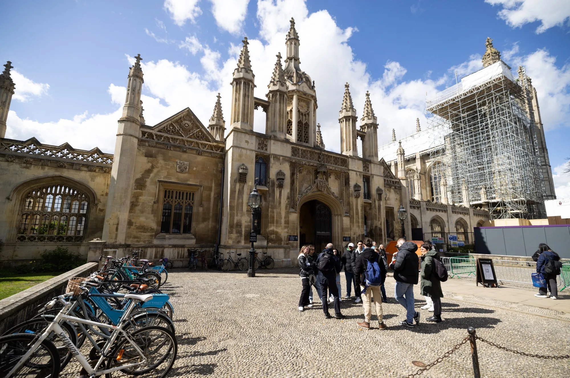 A tour guide speaks to tourists outside the entrance to King's College, University of Cambridge, in Cambridge, UK.