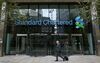 A pedestrian passes the headquarters of Standard Chartered Plc in London, U.K. on Tuesday, Nov. 3, 2015. Standard Chartered Plc dropped the most in more than three years after the lender said it plans to eliminate 17 percent of its workforce, scrap the dividend and tap investors for $5.1 billion as Chief Executive Officer Bill Winters seeks to restore profit growth.