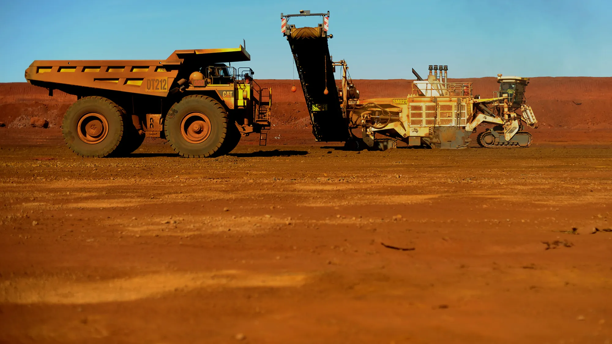 Earth movers receive iron ore deposits from a surface miner in the Cloudbreak Iron Ore mine pit of Fortescue Metals Group at Cloudbreak in Western Australia, on Monday, Jul. 25, 2011.
