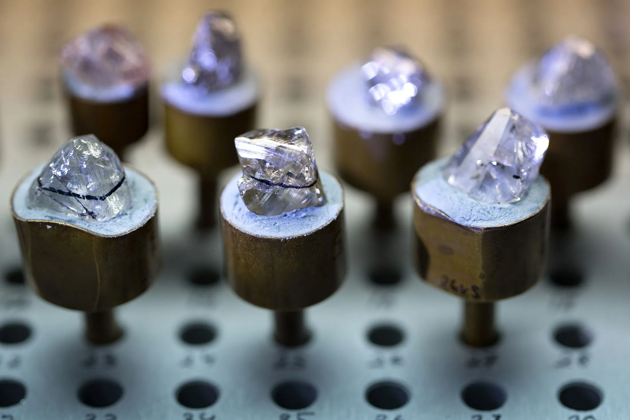 A row of natural diamonds, marked with a defined black line for the laser cutting process, sit on a work surface in Moscow.
