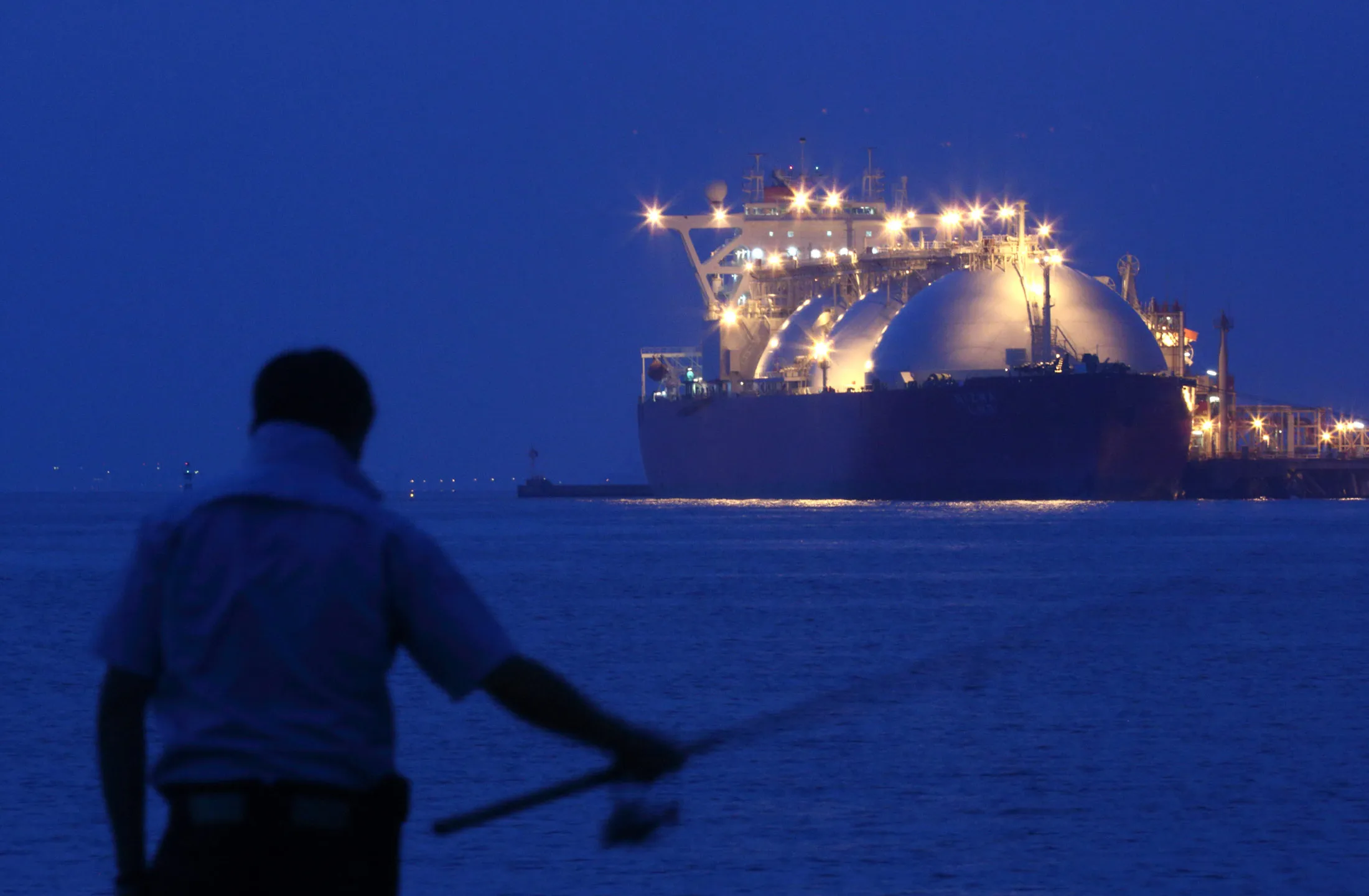 A man fishes in front of a liquefied natural gas (LNG) tanker berthed at Tokyo Electric Power Co.'s (Tepco) Futtsu gas-fired thermal power plant at night in Futtsu, Chiba Prefecture.
