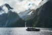 Ferry cruising with mountain and waterfall flowing in fjord at Milford Sound, New Zealand