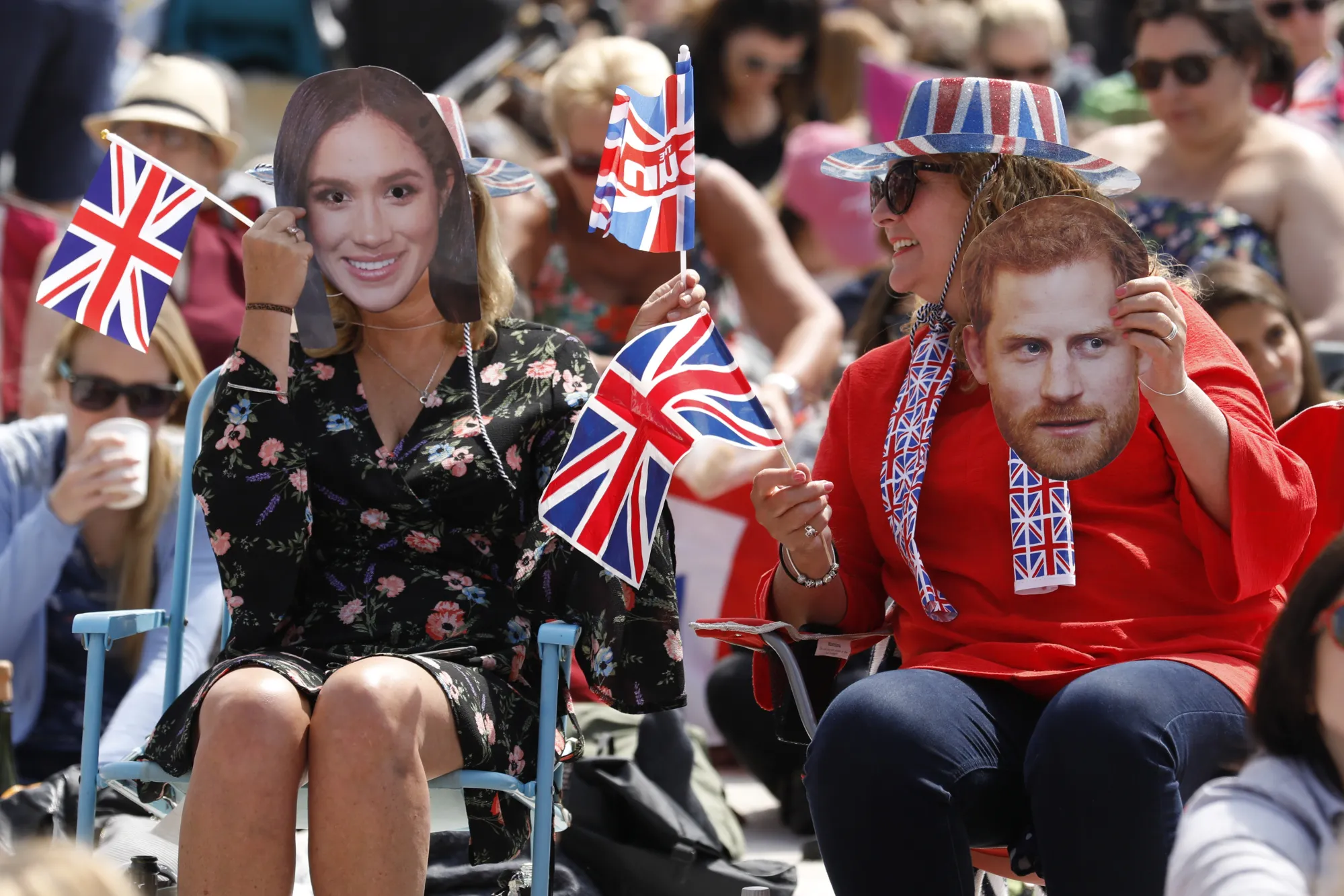 Attendees wearing paper face masks in the likeness of Prince Harry, Duke of Sussex, right, and Meghan Markle, Duchess of Sussex, wave flags as they watch an outdoor television screen showing the wedding of Prince Harry and Meghan Markle,&nbsp;during a royal wedding viewing party in Brighton. on Saturday, May 19.