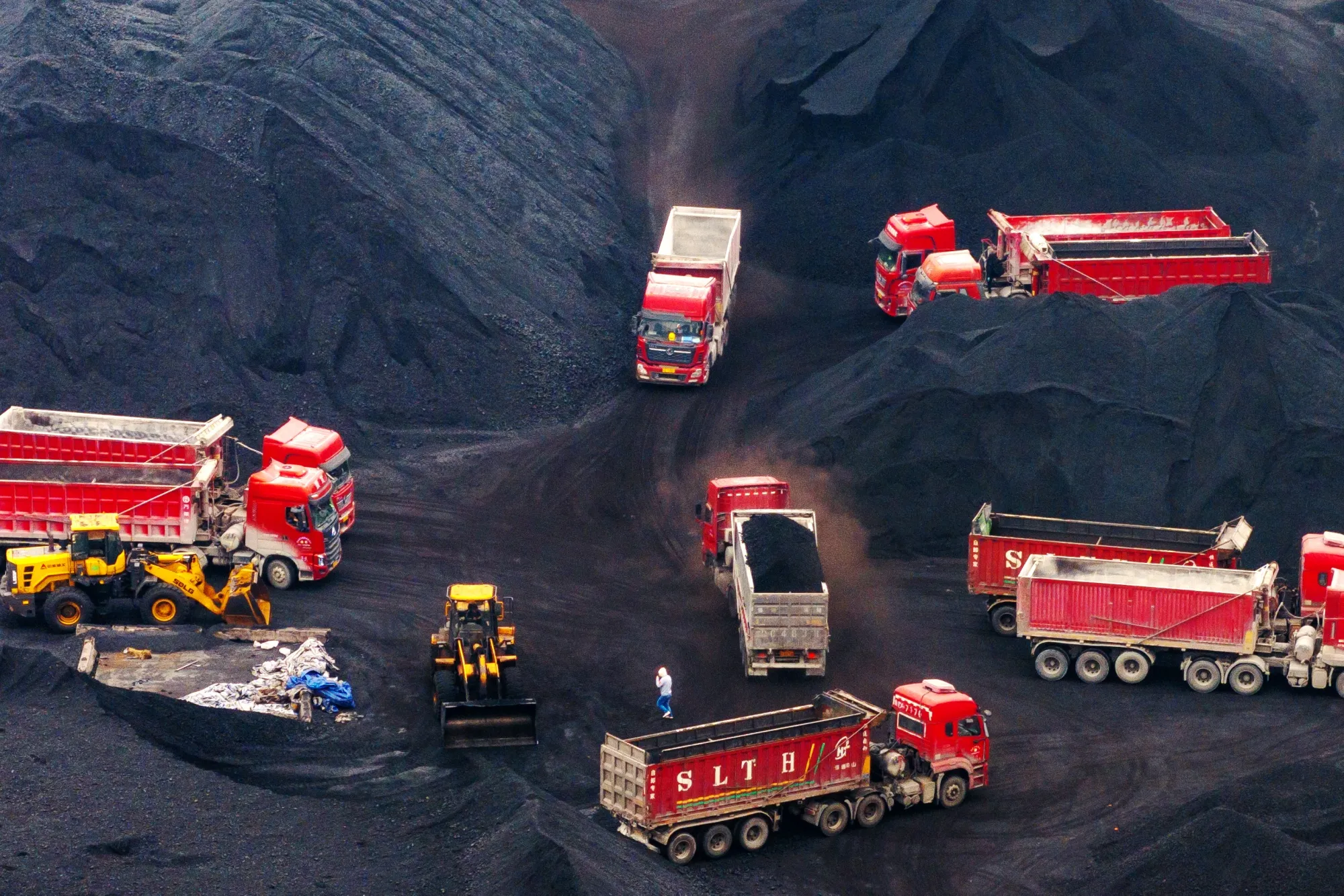 Trucks next to stockpiles of coal at the Guoyuan Port Container Terminal in Chongqing, China.