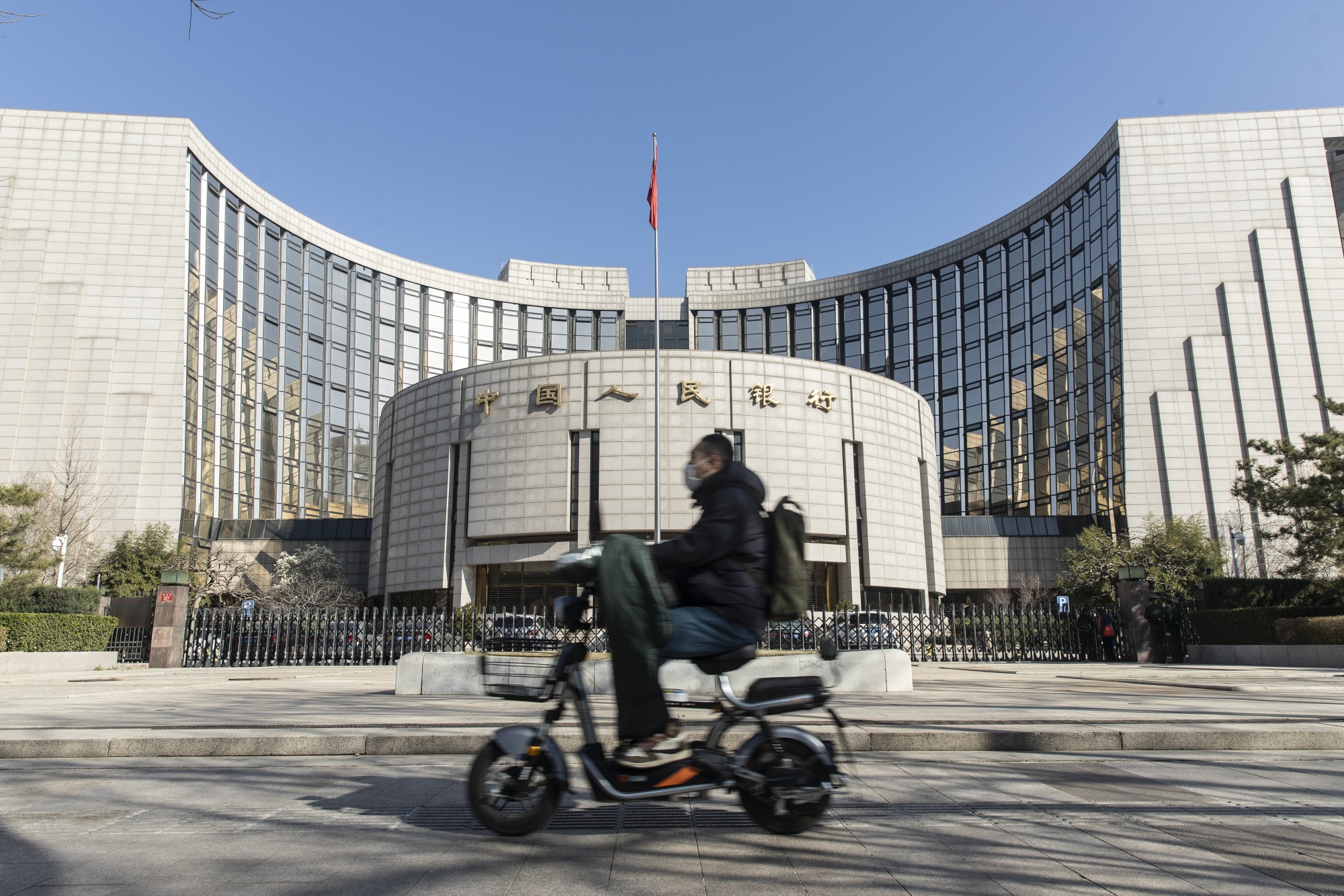 A motorcyclist wearing a protective mask rides past the People's Bank of China building in Beijing.